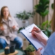 A woman writing down on a clipboard with another woman talking to her blurred in the distance.