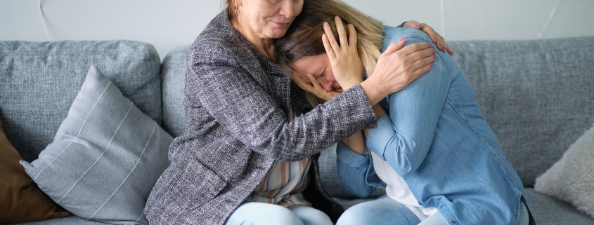 An elderly woman hugging and comforting a younger woman crying.