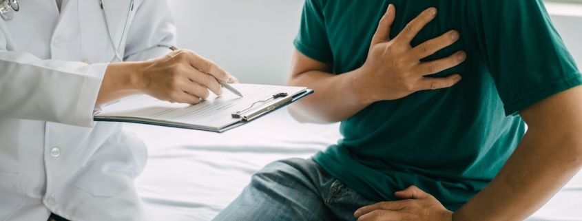 Man grasping his heart while doctor writes down on clipboard
