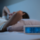 a woman lying on a bed with a digital clock